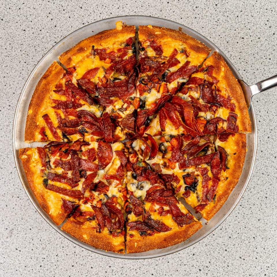 A sliced Santorini Pizza & Pasta pizza with pepperoni, cheese, and olives on a metal pan.