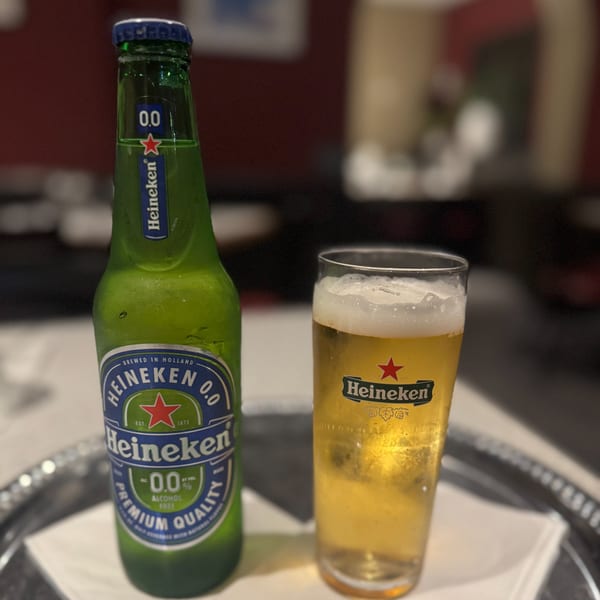 A cold bottle of Heineken 0.0 and a glass of the non-alcoholic beer on a silver tray.
