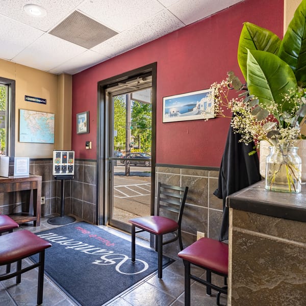 The entrance of Santorini Pizza & Pasta, with a red wall, map of Greece, and a welcome mat.