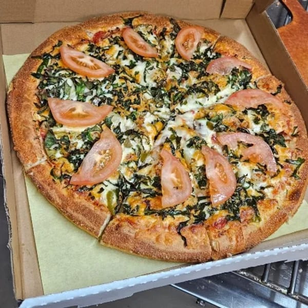 A whole Santorini Pizza & Pasta pizza, topped with spinach, cheese, and tomato slices, in a cardboard box.