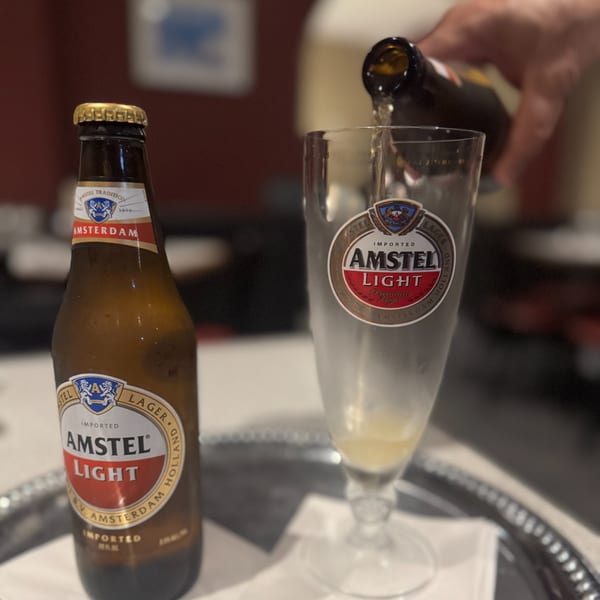 A bottle of Amstel Light beer next to a glass being filled with beer on a silver tray.