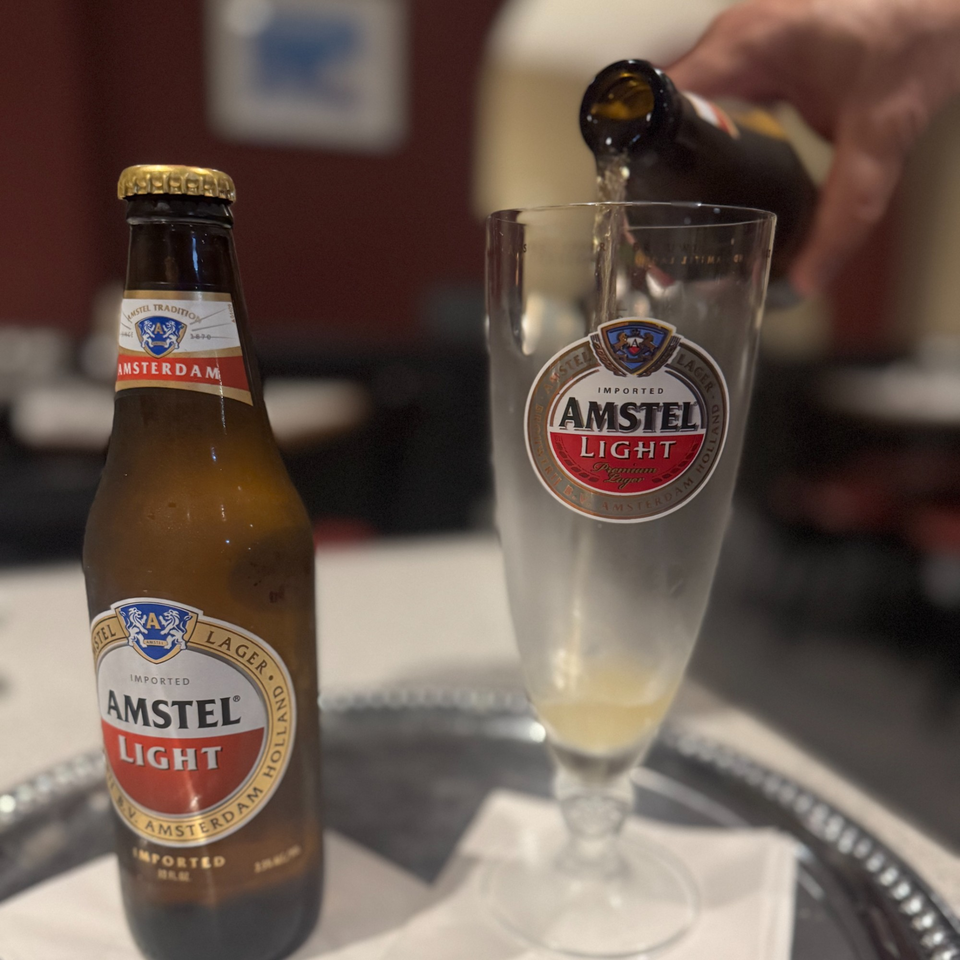 A bottle of Amstel Light beer next to a glass being filled with beer on a silver tray.