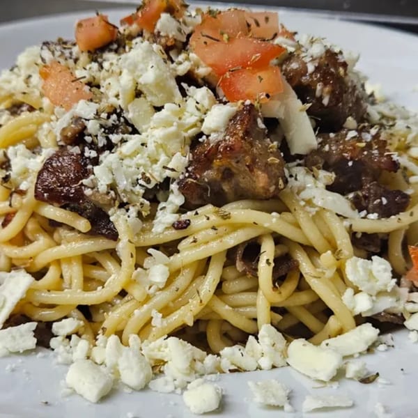 Spaghetti with meat, crumbled feta cheese, diced tomatoes, and herbs on a white plate.