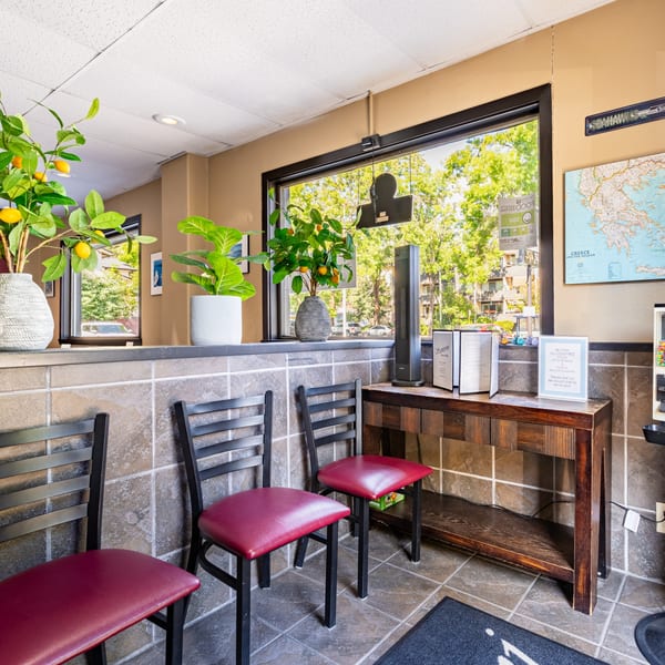 Waiting area of Santorini Pizza & Pasta with red-seated chairs, plants, and a Greece map.
