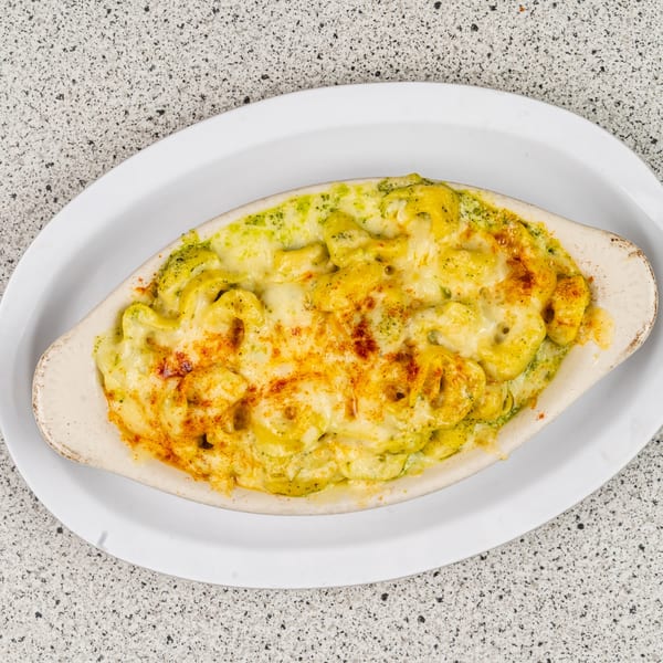 Baked pasta dish with green sauce and melted cheese, sprinkled with paprika, in an oval white dish.