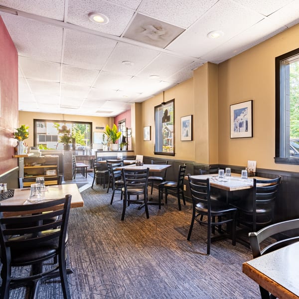 Interior of Santorini Pizza & Pasta, showing empty dining tables with black chairs and warm lighting.
