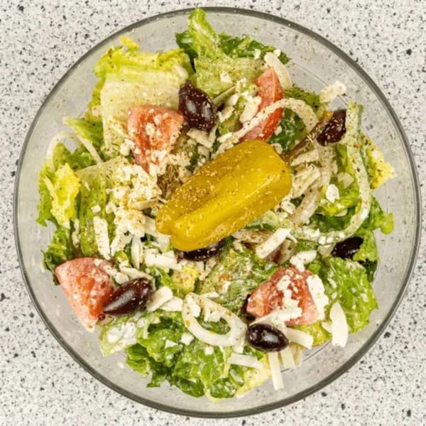 A vibrant Santorini Pizza & Pasta salad with lettuce, tomatoes, olives, onions, feta, and a pepperoncini.