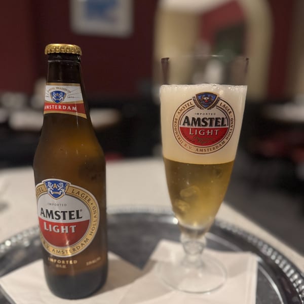 A bottle of Amstel Light beer next to a glass filled with the same beer on a silver tray.
