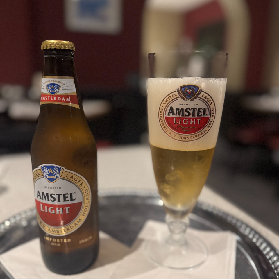 A bottle of Amstel Light beer next to a glass filled with the same beer on a silver tray.