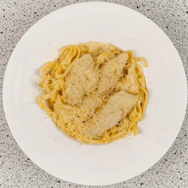 Creamy chicken alfredo pasta with grated cheese on a white plate from Santorini Pizza & Pasta.