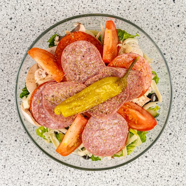Overhead view of a Santorini Pizza & Pasta antipasto salad with salami, pepperoni, tomatoes, and a pepperoncini.