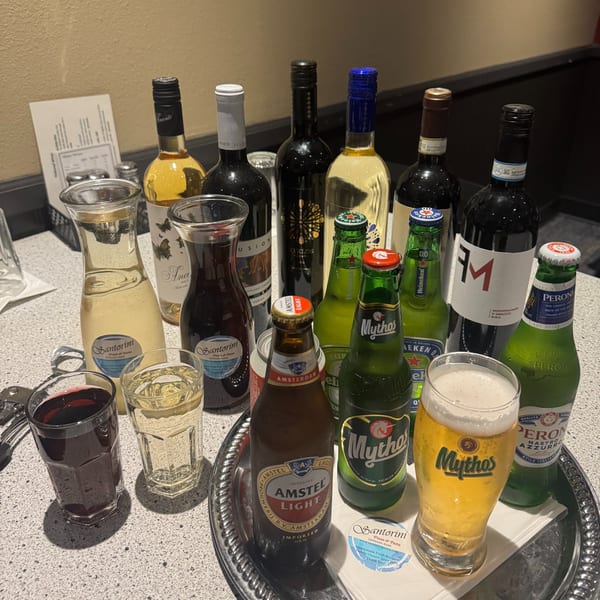 A table laden with various bottles of wine, beer, and glasses of beverages at Santorini Pizza & Pasta.