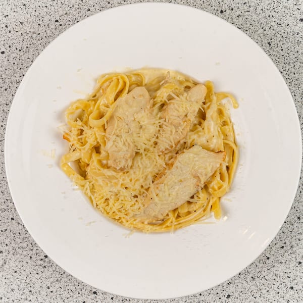Chicken Alfredo pasta with fettuccine noodles and grated Parmesan cheese on a white plate.