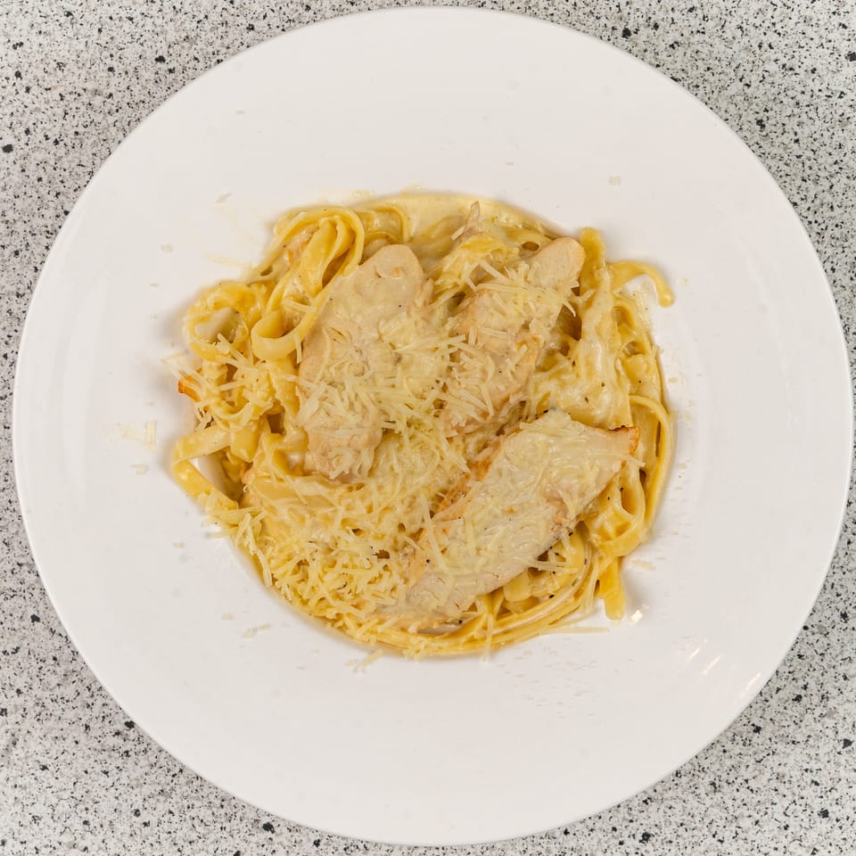 Chicken Alfredo pasta with fettuccine noodles and grated Parmesan cheese on a white plate.