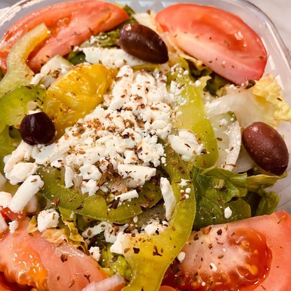 A vibrant Greek salad with lettuce, tomatoes, bell peppers, olives, and crumbled feta cheese.